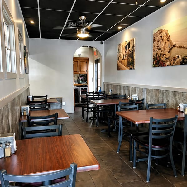 Empty restaurant dining room with wooden tables, black chairs, and landscape art on the walls.
