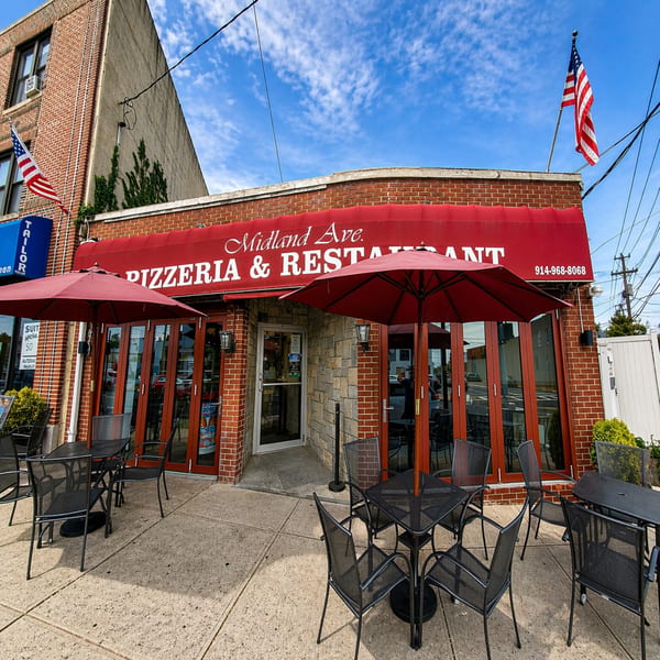 Midland Ave. Pizzeria & Restaurant exterior with red awning, outdoor seating, and American flags.