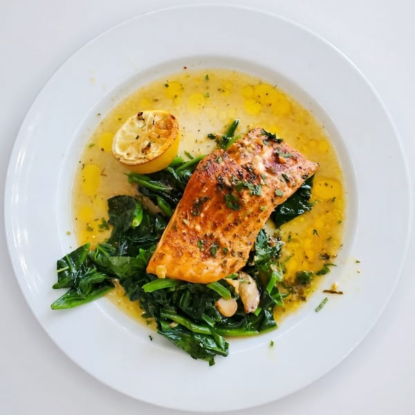 Pan-seared salmon with sautéed spinach, roasted lemon, and a buttery herb sauce on a white plate.