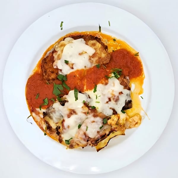 Eggplant Parmesan with melted mozzarella, rich tomato sauce, and fresh parsley on a white plate.