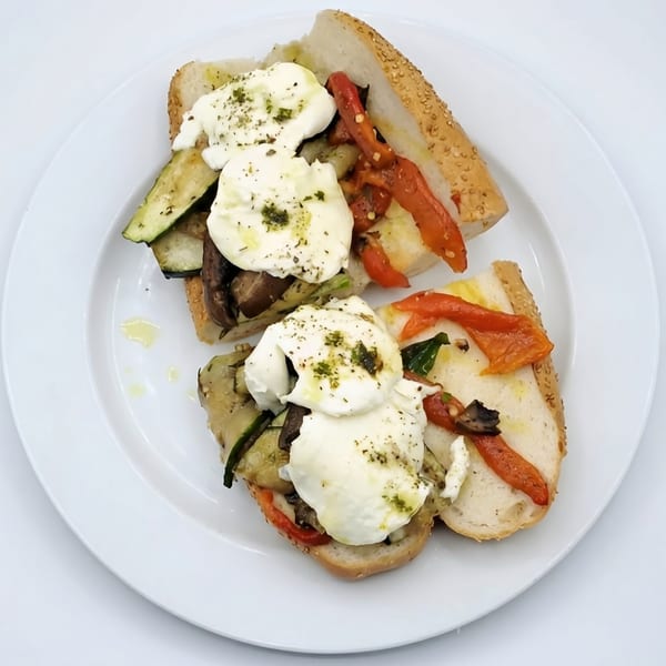 Two open-faced sandwiches with roasted vegetables, fresh mozzarella, and herbs on a white plate.